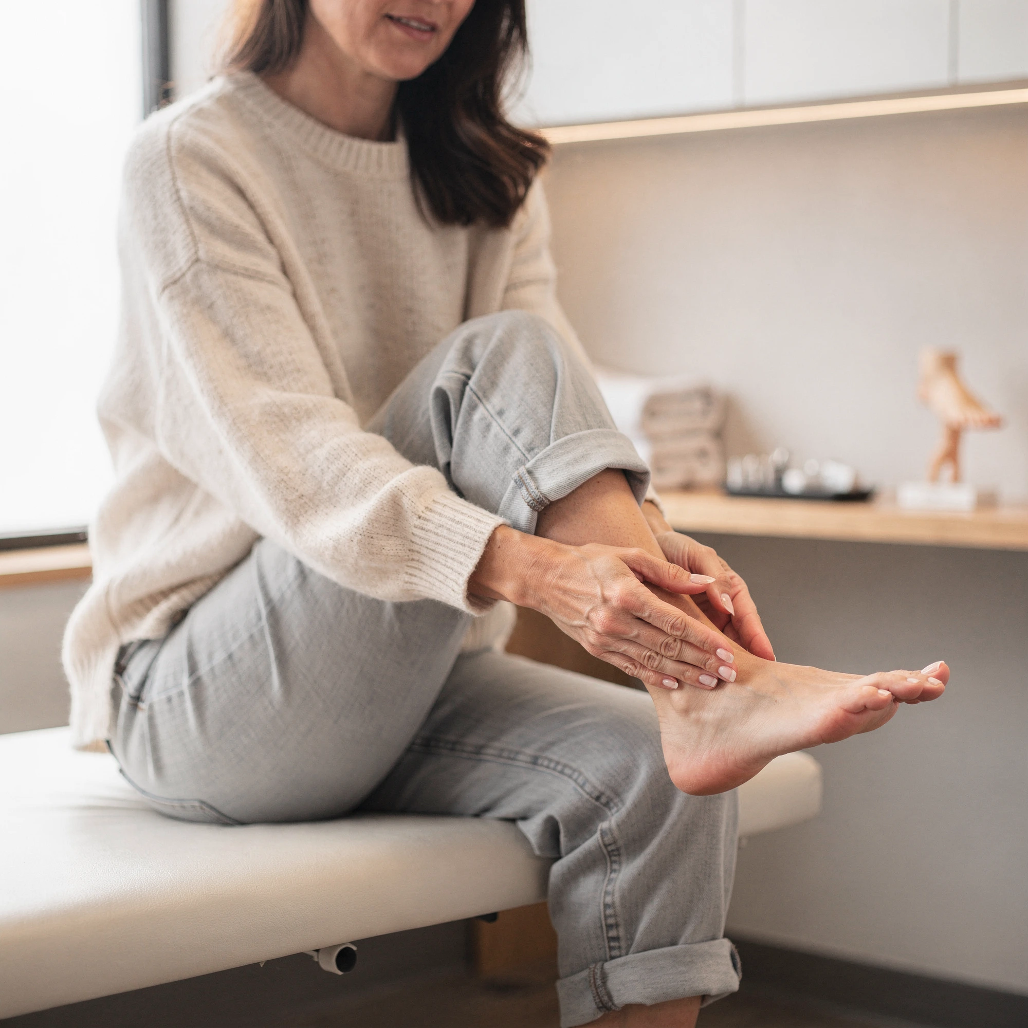 Woman sitting on an exam table examining her foot and ankle